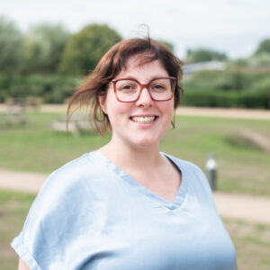 Kaat Wouters poseert met bril en lichtblauwe blouse. Op de achtergrond is wazig een park te zien.