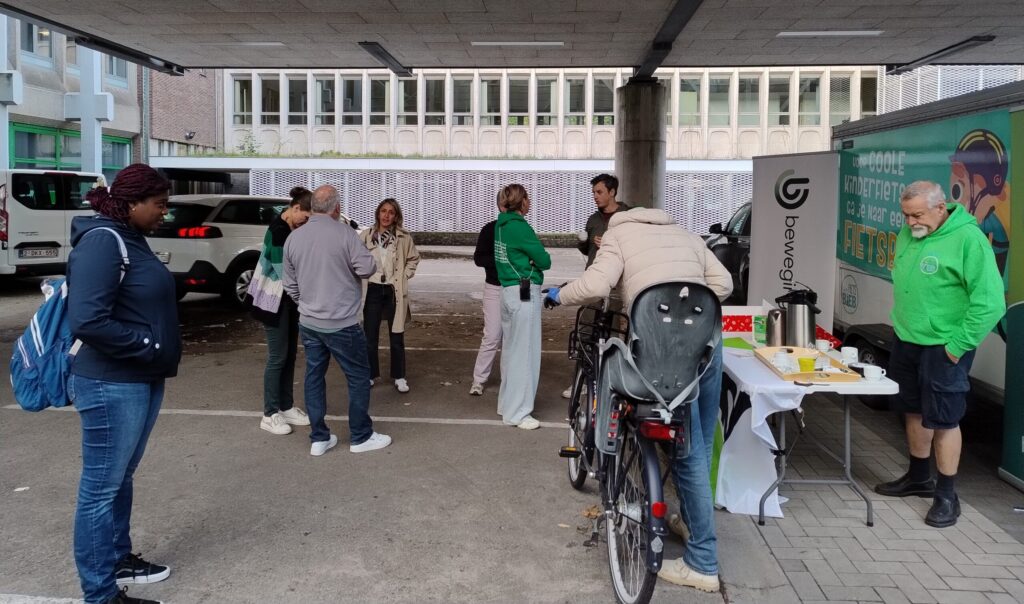 Enkele mensen staan op de parking van ACV in Sint-Niklaas. Ze slaan een babbeltje en sommigen drinken koffie. Eén fietster wacht om haar fiets te laten repareren.