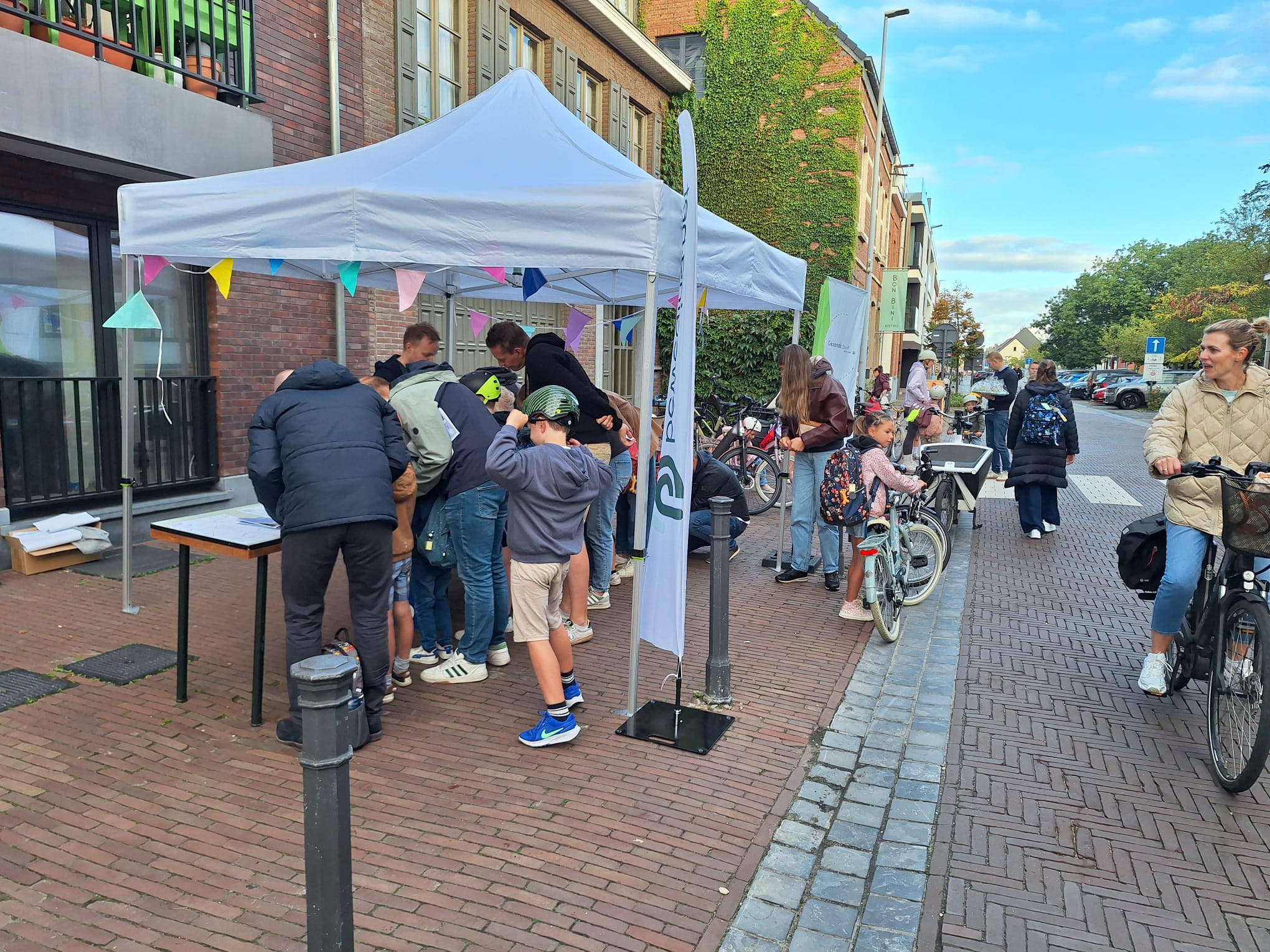 Een partytent staat opgesteld op het voetpad met enkele beachvlaggen van beweging.net en CM Gezonde Buurt.
