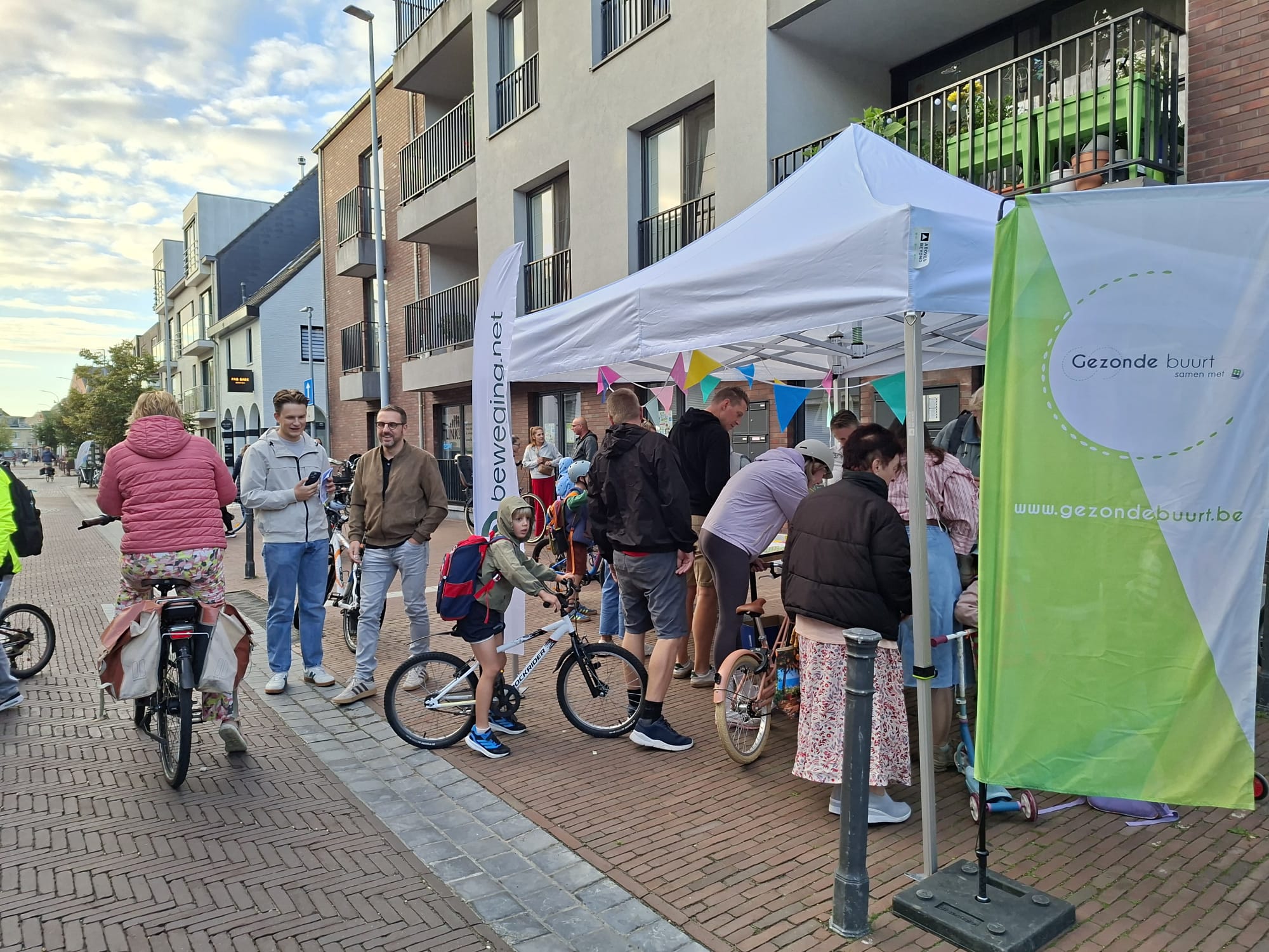 Een partytent staat opgesteld op het voetpad met enkele beachvlaggen van beweging.net en CM Gezonde Buurt.