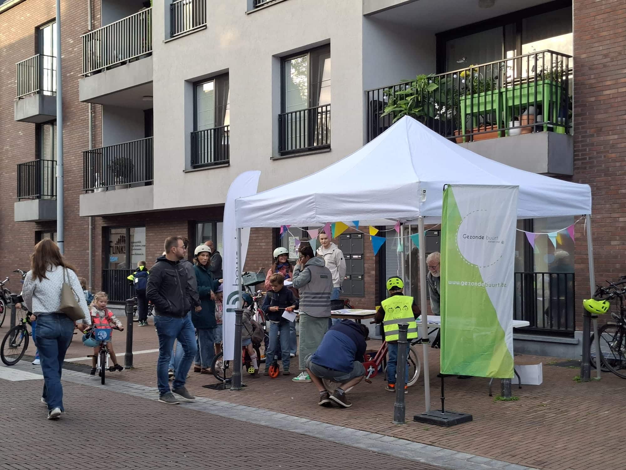Een partytent staat opgesteld op het voetpad met enkele beachvlaggen van beweging.net en CM Gezonde Buurt.